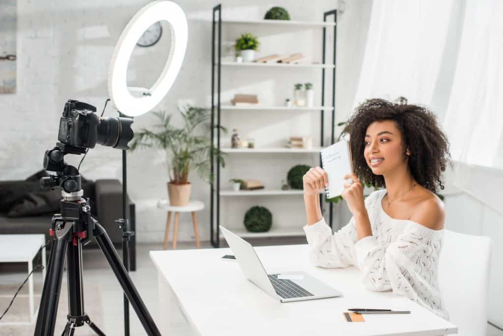 happy african american video blogger in braces holding notebook with influencer marketing lettering